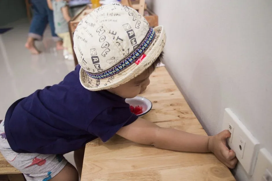 A small child reaching toward a low kitchen cabinet where cleaning powder is stored, illustrating a household poisoning hazard