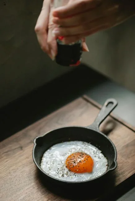 A well-seasoned black cast iron skillet on a wooden kitchen counter next to a bottle of dish soap and a sponge