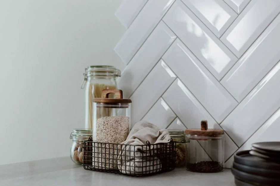 Glass storage jars of white sugar, table salt, and white rice sealed with lids on a wooden pantry shelf