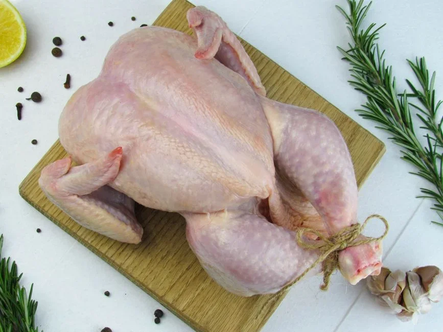 Raw whole chicken being rinsed under running water in a stainless steel kitchen sink, demonstrating the unsafe poultry washing habit