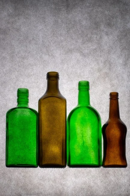 Brown opaque bottle of 3% hydrogen peroxide on a kitchen counter next to a spray bottle, a microfiber cloth, and a wooden cutting board