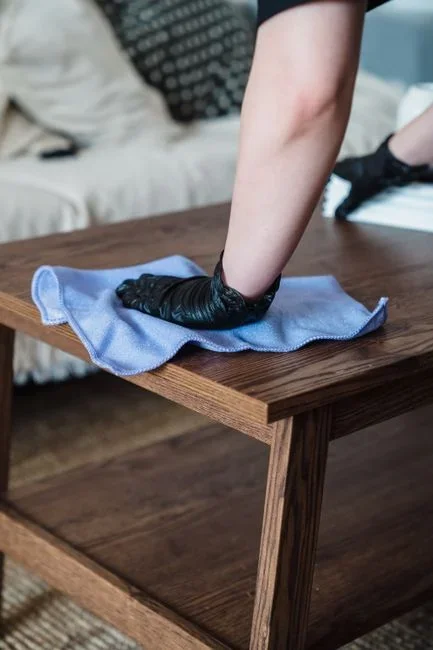 Hands wiping a wooden cutting board with hydrogen peroxide and a paper towel after washing it with soapy water at a kitchen sink