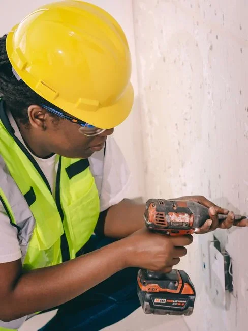 Person drilling a wide vertical hole into a tree stump with a cordless drill and spade bit, sawdust visible