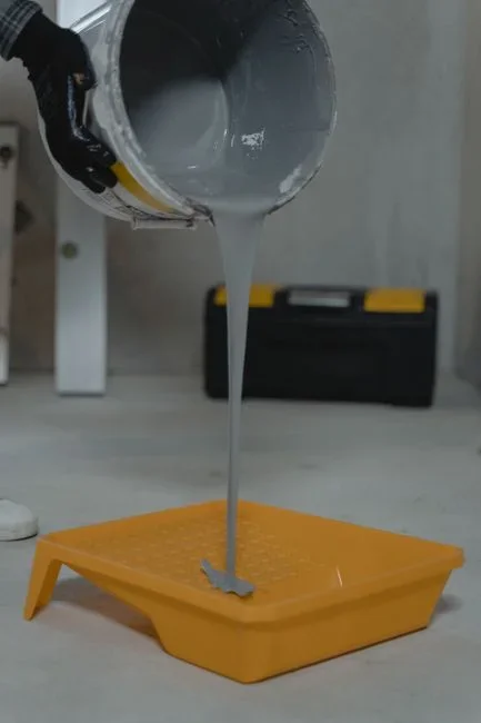 Person pouring gray concrete mix into a gallon plastic zip bag on a wooden table outdoors