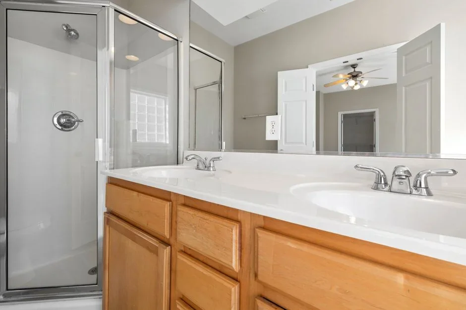 Heavily fogged bathroom mirror above a vanity with a running white ceiling exhaust fan visible in the upper corner of the frame