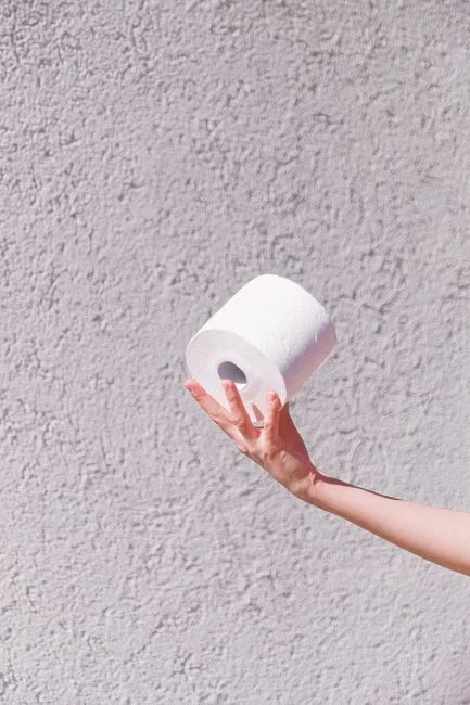 Hand holding a single square of white toilet tissue flat against a ceiling bathroom exhaust fan grille to test airflow