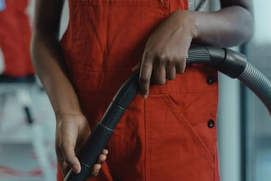 Person using a shop vacuum hose with a knee-high nylon stocking inserted in the wand to remove lady beetles from an interior window frame corner