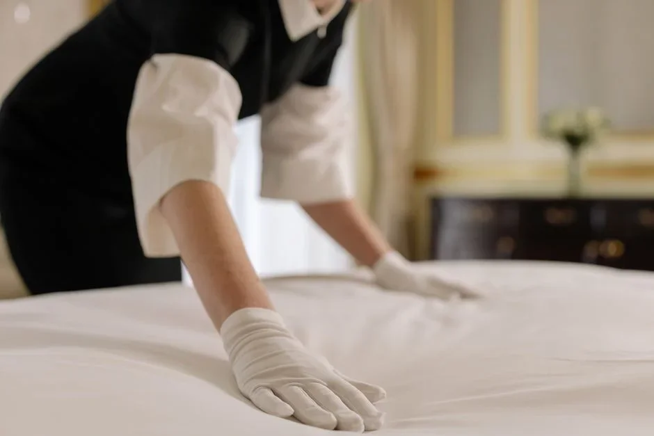 Gloved hands pulling back a fitted sheet to inspect the dark piping and seam of a mattress corner with a flashlight
