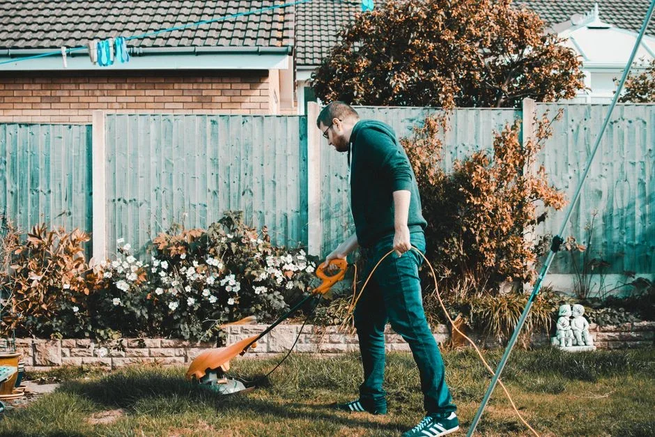 Homeowner in long pants tucked into tall socks trimming overgrown weedy brush where a mown suburban lawn meets a wooded fence line