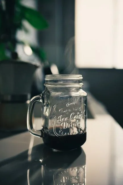 Large glass mason jar of dark coffee concentrate steeping with coarse coffee grounds on a refrigerator shelf