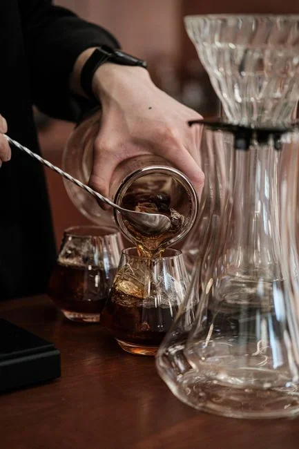 Cold brew concentrate being diluted with water and poured over ice in a tall glass, showing the one-to-one dilution