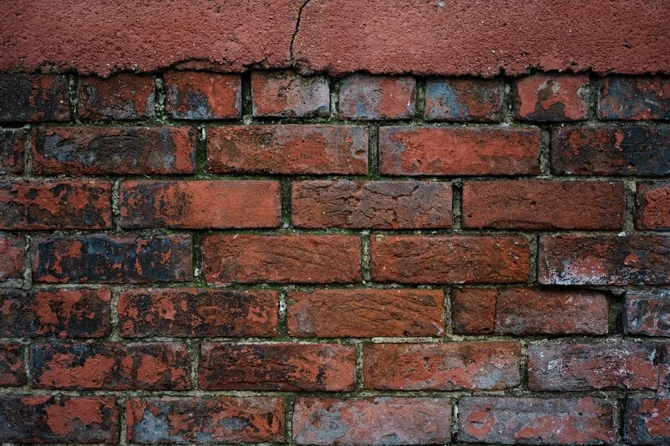 Close-up of a weathered red brick wall with crumbling white lime mortar joints and several bricks with spalled faces