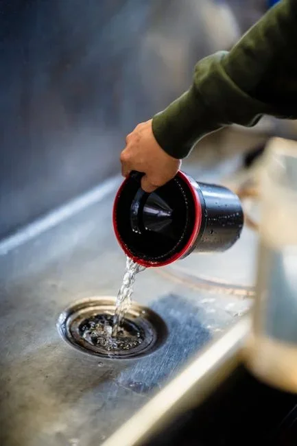 Hands lifting the cylindrical mesh filter out of the bottom of an open dishwasher tub