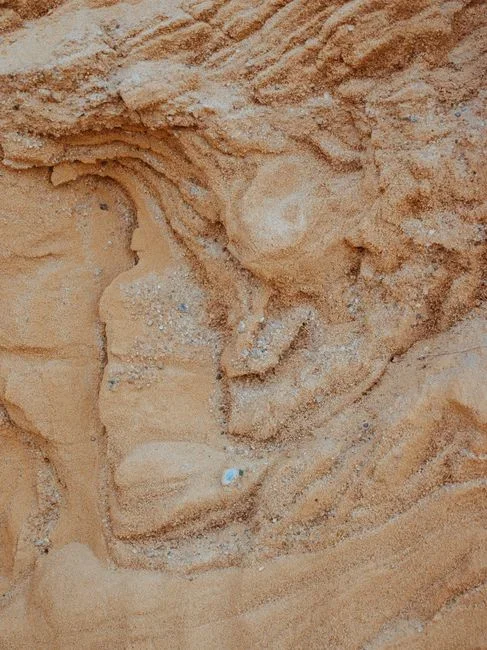 Cutaway view of a homemade five-gallon bucket water filter showing layers of gravel, coarse sand, fine sand, and charcoal, with cloudy water poured in at the top