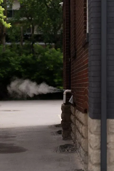 Outdoor dryer vent hood on house siding with its flap propped open and warm exhaust escaping while the dryer runs