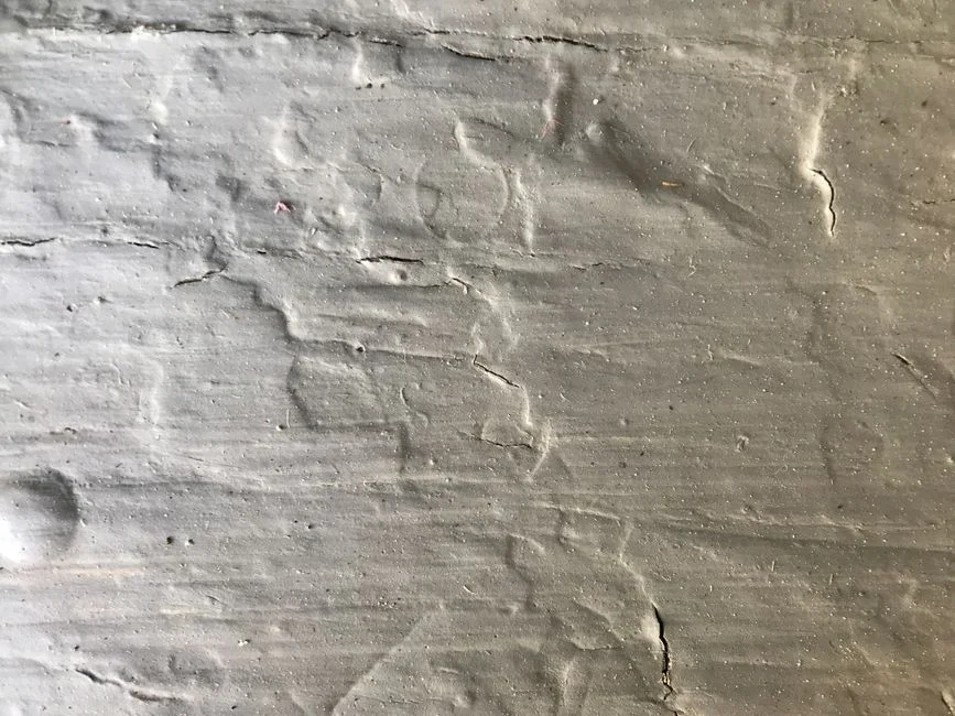 Close-up of a thin vertical crack running down a gray poured concrete basement wall with a tape measure held beside it