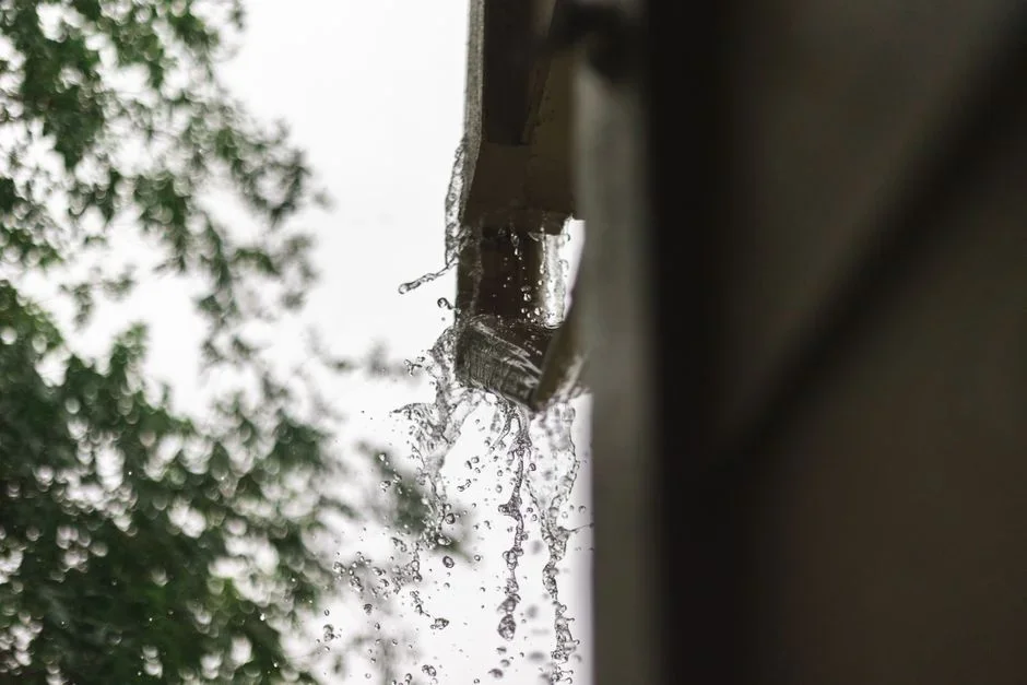Rainwater overflowing from a clogged leaf-filled gutter and splashing down against a house foundation during a storm