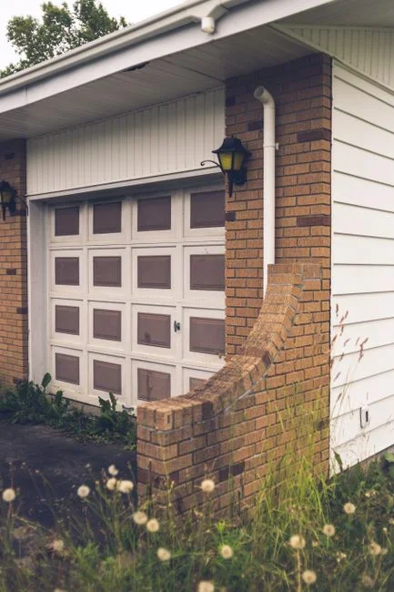 Homeowner attaching a corrugated plastic downspout extension to redirect roof water away from a brick house foundation