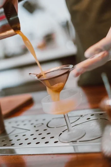 Cooled golden used frying oil being poured through a fine mesh sieve lined with cheesecloth into a clean glass storage jar on a kitchen counter