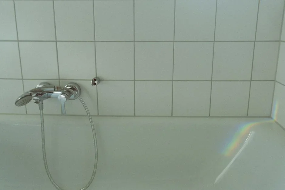 Moldy black silicone caulk in the corner joint where a tiled shower wall meets a white bathtub