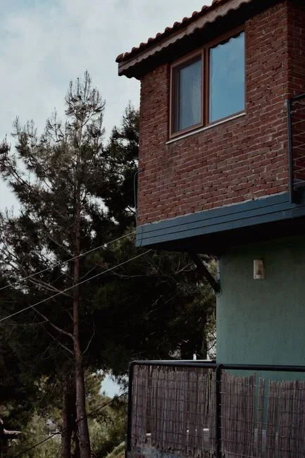 Small vertical-axis wind turbine bolted to the roof ridge of a suburban house surrounded by tall trees