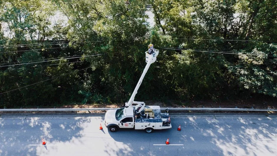 Utility lineworker in hard hat and fall-arrest harness working on an overhead power line from a bucket truck