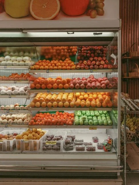 Open refrigerator crisper drawer showing bagged leafy greens and broccoli stored separately from a bowl of apples on the shelf above