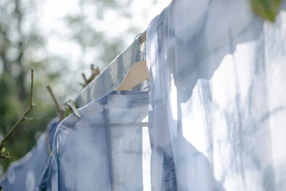 Cotton bedsheets and towels hanging on an outdoor clothesline in a sunny backyard with wooden clothespins