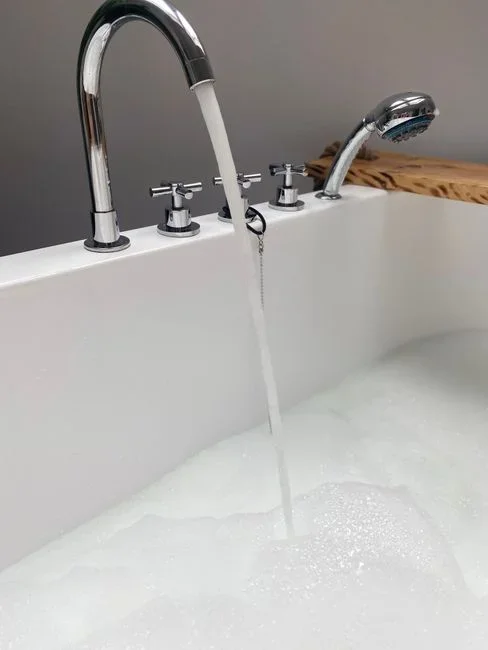 Showerhead unscrewed and set aside while water runs in a strong stream from the bare chrome shower arm into a bathtub