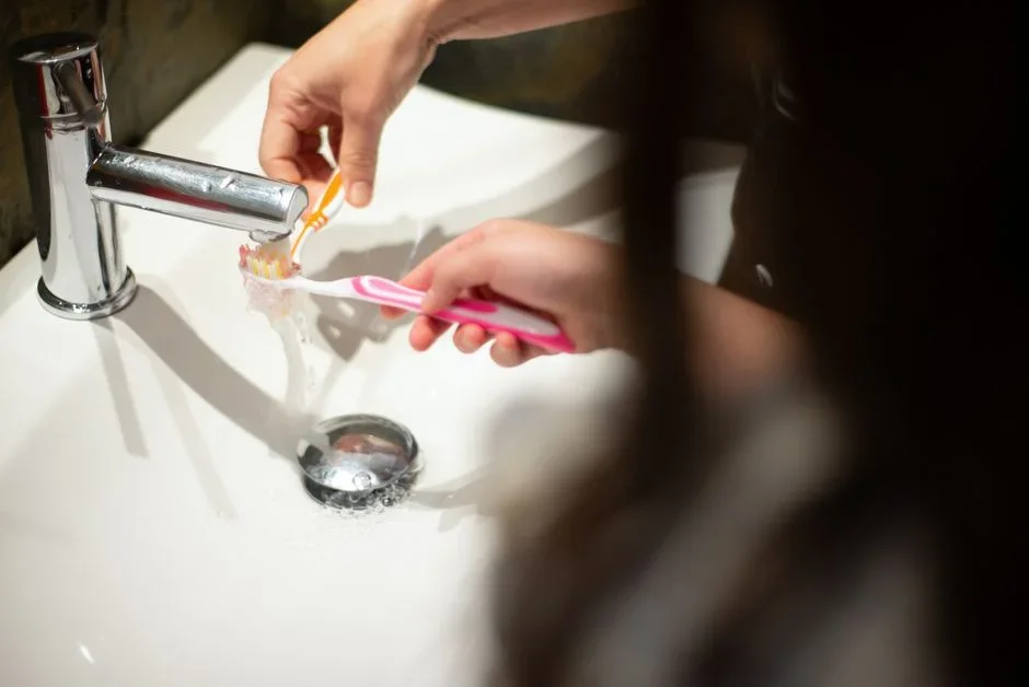 Close-up of a showerhead face crusted with white mineral scale being scrubbed with an old toothbrush over a sink