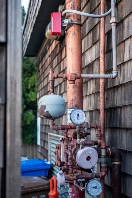 Brass water pressure test gauge screwed onto an outdoor hose bibb with the dial needle clearly visible against a house wall