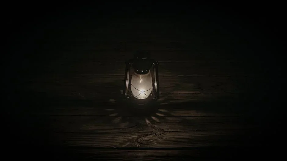 Antique brass hurricane oil lamp with clear glass chimney burning on a wooden kitchen table during a nighttime power outage