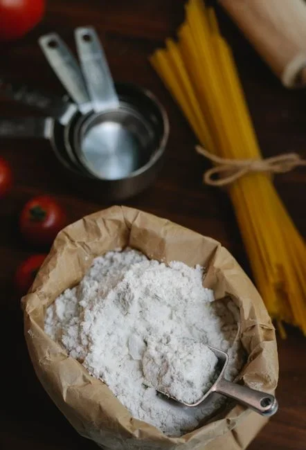 Hands sealing a five-pound paper bag of flour inside a large zip-top freezer bag beside an open chest freezer with a dial thermometer inside
