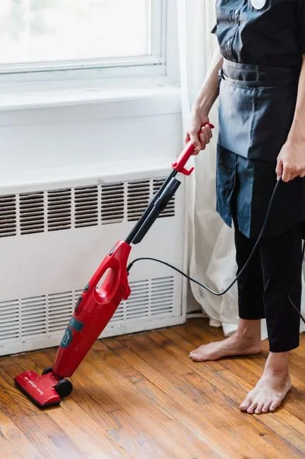 Person using a narrow crevice vacuum attachment along the back seam and corner of an emptied wooden pantry shelf