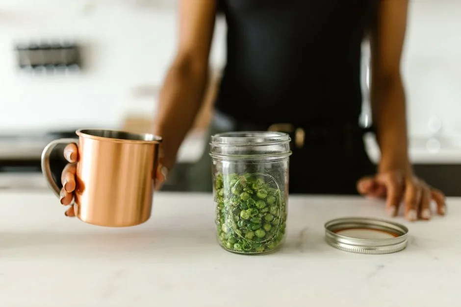 Home kitchen counter with fresh green beans, glass canning jars, flat lids and a stovetop pressure canner ready for processing