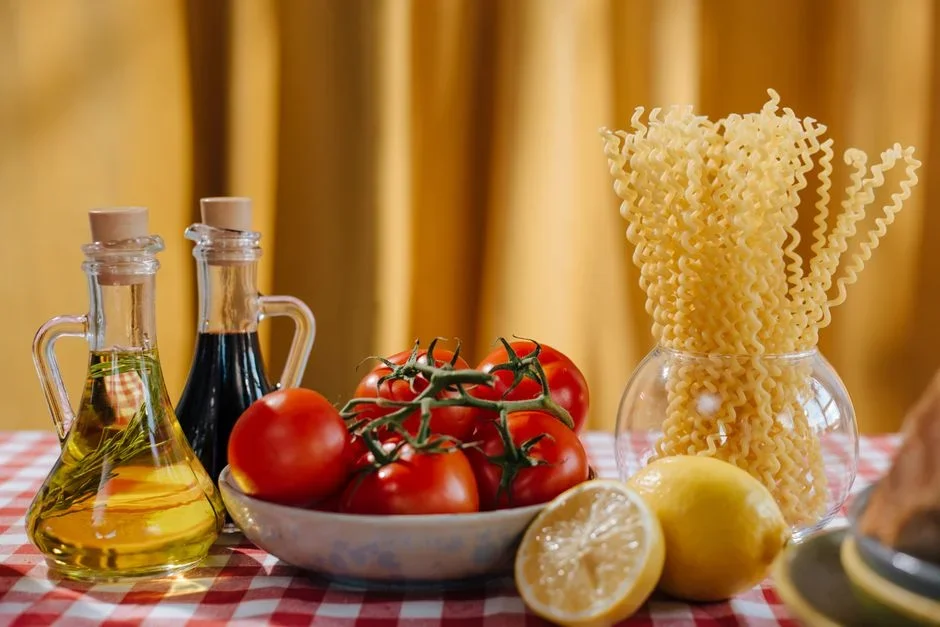 Bowl of ripe garden tomatoes beside a bottle of lemon juice and a measuring spoon on a wooden kitchen table