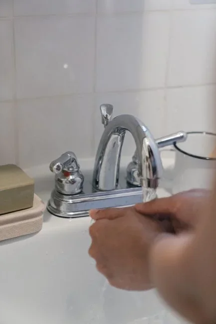 Person wearing safety goggles and rubber gloves rinsing an eye under gently running water at a utility sink