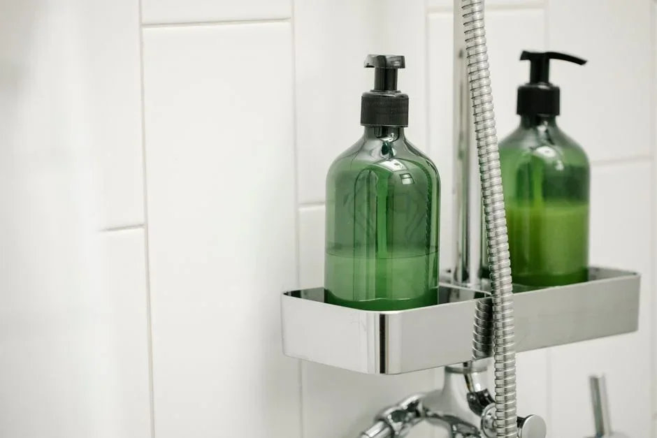 Bottle of chlorine bleach and a bottle of white vinegar standing side by side on a bathroom floor next to a shower