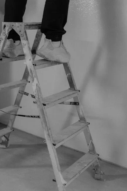 Homeowner on a step ladder unscrewing the white grille cover of a ceiling bathroom exhaust fan