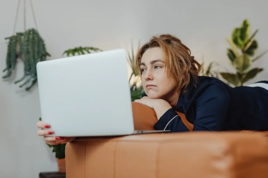 Frustrated woman on a couch looking at a laptop showing a buffering video spinner in a living room