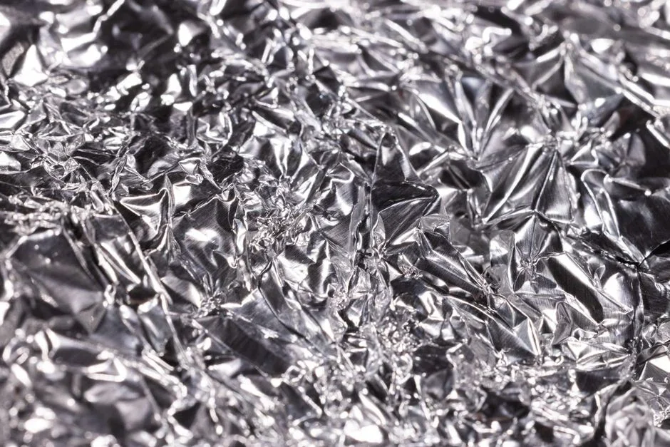 Sheet of crumpled aluminum foil propped behind a black Wi-Fi router antenna on a wooden shelf