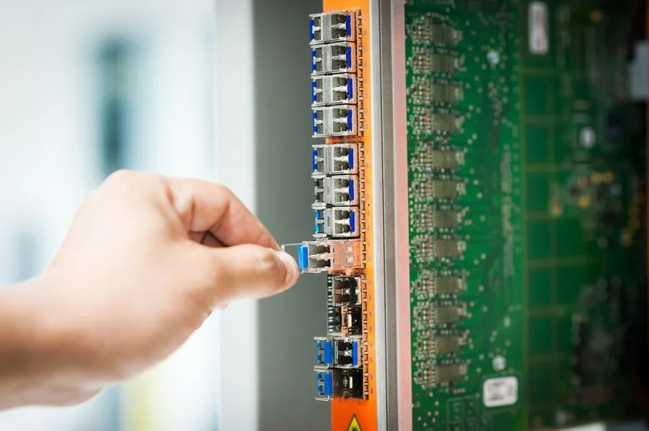 Hands plugging a flat white Ethernet cable into the back of a smart TV mounted on a living room wall