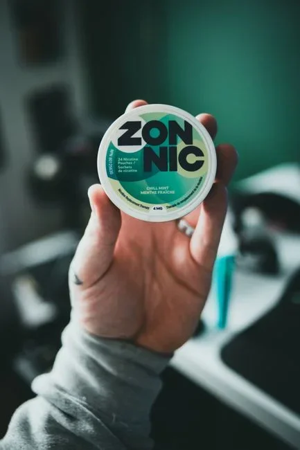 Close-up of the printed label on the back of a smoke alarm showing sensor type and date of manufacture, held in a person's hand under kitchen light
