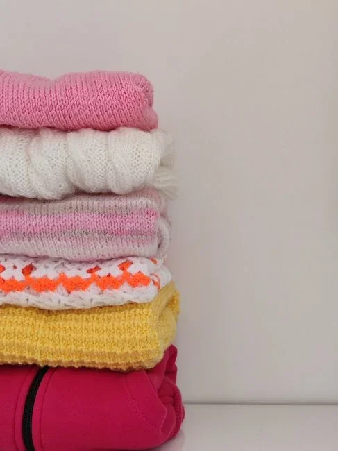 White mothballs spilling from an open glass jar onto a wooden closet shelf next to folded sweaters
