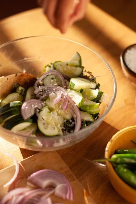 Hands grating fresh green zucchini into a glass bowl next to a steamer basket on a stovetop