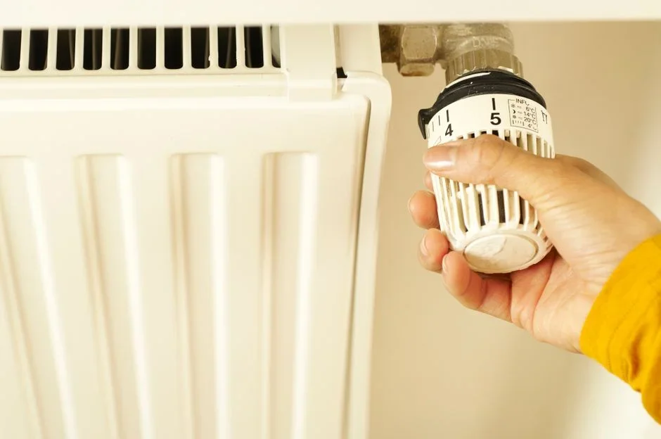 Person removing the access panel on a residential gas water heater to reach the thermostat dial in a basement utility area