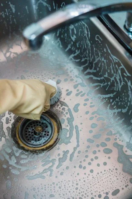 Close-up of black rubber splash guard flaps inside a stainless steel kitchen sink drain opening, coated with grey food film