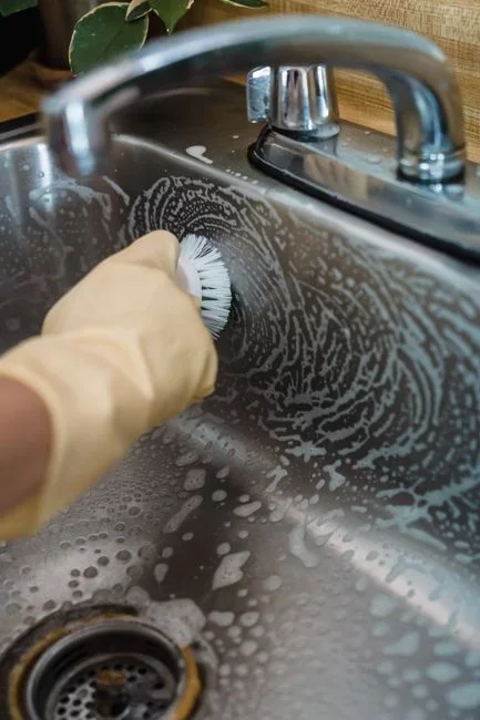 Bottle of chemical drain cleaner standing on a kitchen counter next to a stainless steel sink with the disposal opening visible