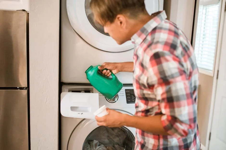 Person kneeling on laundry room floor draining a front-load washer's drain pump hose into a shallow pan next to an open access panel