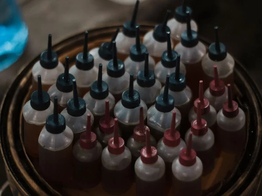 Hand squeezing blue food coloring from a small bottle into an open toilet tank, porcelain lid resting on a towel beside it